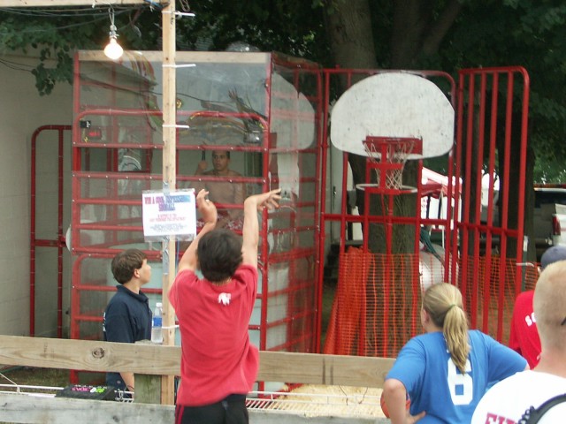 Fair goers shoot basketballs, trying to dunk a member.
